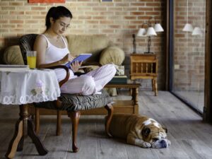 woman sitting in chair reading on ipad at home with dog at her feet
