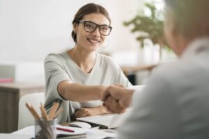 woman with glasses shaking hands with person on other side of table