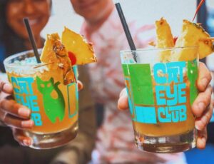 two people holding tiki bar cocktails and showing them to the camera