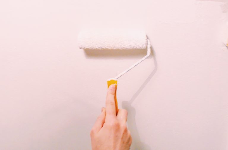 person's hand painting pink paint onto wall