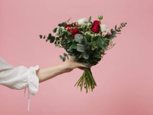 arm of woman holding beautiful bouquet of flowers roses pink background