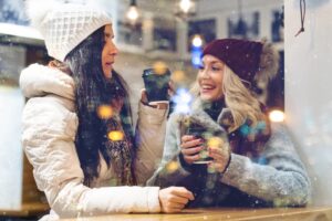 two women sipping on warm drinks inside a cafe