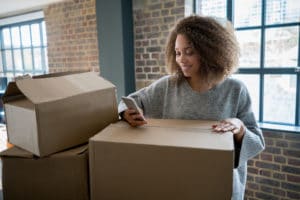 woman on her phone smiling while resting arm on moving box
