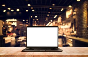 blank laptop screen sitting on wooden table with lights in the background