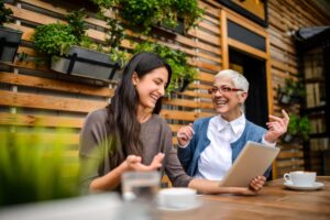 two women sitting outdoors at table looking at piece of paper and smiling