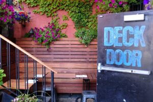 outdoor patio with greenery and door with sign reading "deck door"