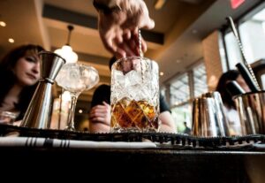 bartender mixing drink on bar with customer in background