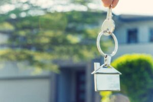 Hand holding house key in front of a large house
