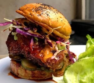 close up of juicy burger on white plate with lettuce next to it