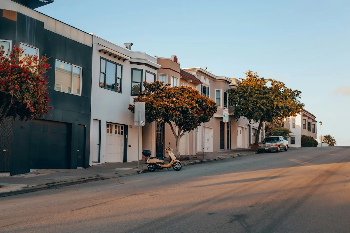 Residential street in a San Francisco neighborhood at sunset, lined with pastel-colored homes and a parked scooter โ illustrating everyday renter life and housing styles across the city in 2025.