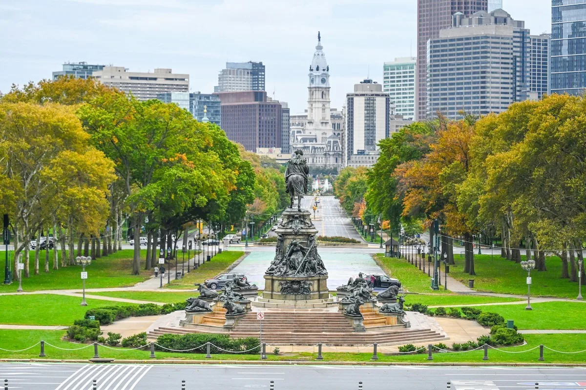 View of the Benjamin Franklin Parkway in Philadelphia with the Washington Monument Fountain in the foreground and City Hall in the distance, showcasing the cityโs skyline and cultural landmarks featured in โIs Philadelphia Affordable for Renters in 2025.โ