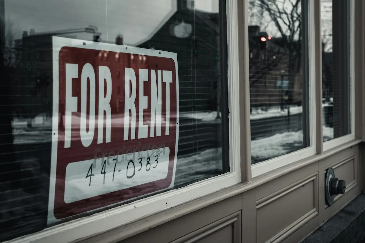 A For Rent sign displayed in the window of an apartment building during winter, representing rental availability in competitive housing markets